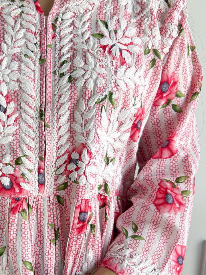 Close-up of a floral patterned fabric with pink flowers and green leaves on a white background.